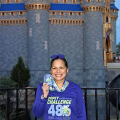 A woman holding up her medal in front of a castle.