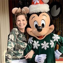 A woman standing next to mickey mouse wearing a christmas hat.