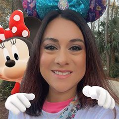 A woman with minnie mouse ears on and her hands in front of her face.