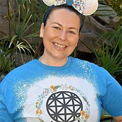 A woman wearing a blue shirt and mickey mouse ears.